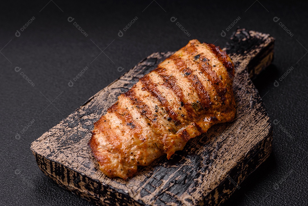 Delicioso filé de frango grelhado fresco com especiarias e ervas em um fundo escuro de concreto. Um prato cozido no fogo