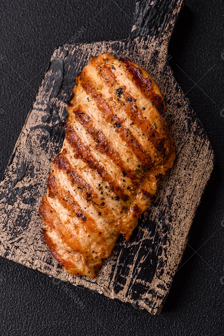 Delicioso filé de frango grelhado fresco com especiarias e ervas em um fundo escuro de concreto. Um prato cozido no fogo