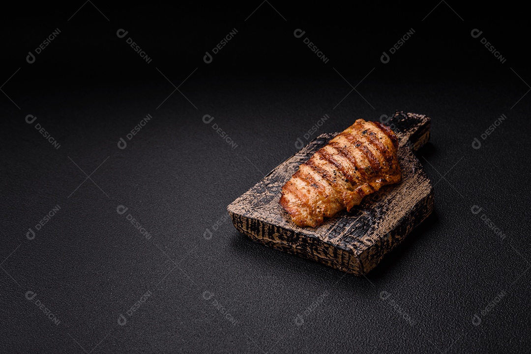 Delicioso filé de frango grelhado fresco com especiarias e ervas em um fundo escuro de concreto. Um prato cozido no fogo