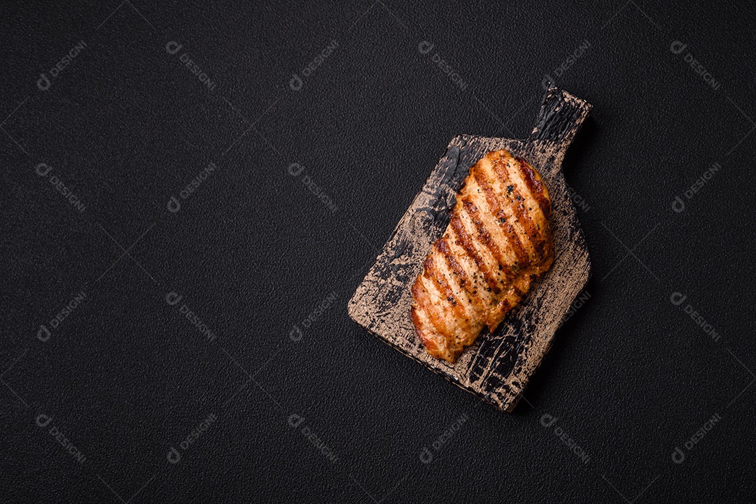 Delicioso filé de frango grelhado fresco com especiarias e ervas em um fundo escuro de concreto. Um prato cozido no fogo