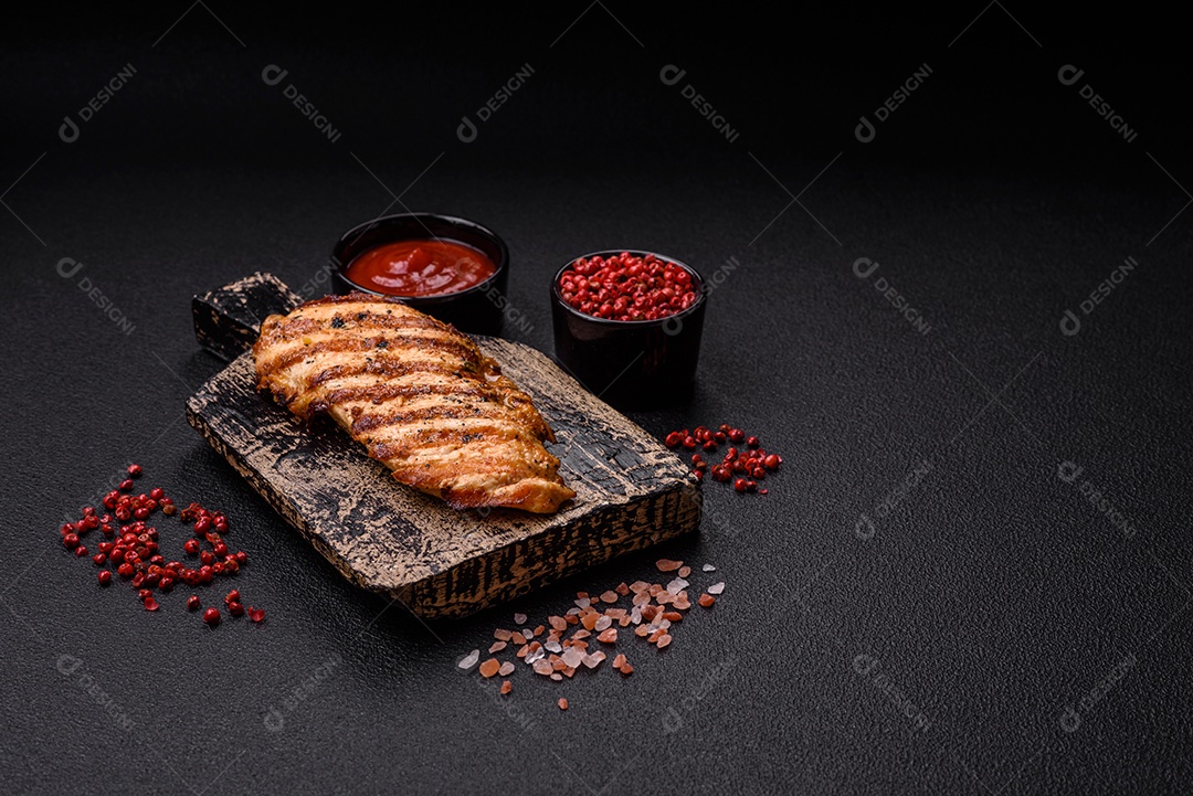 Delicioso filé de frango grelhado fresco com especiarias e ervas em um fundo escuro de concreto. Um prato cozido no fogo