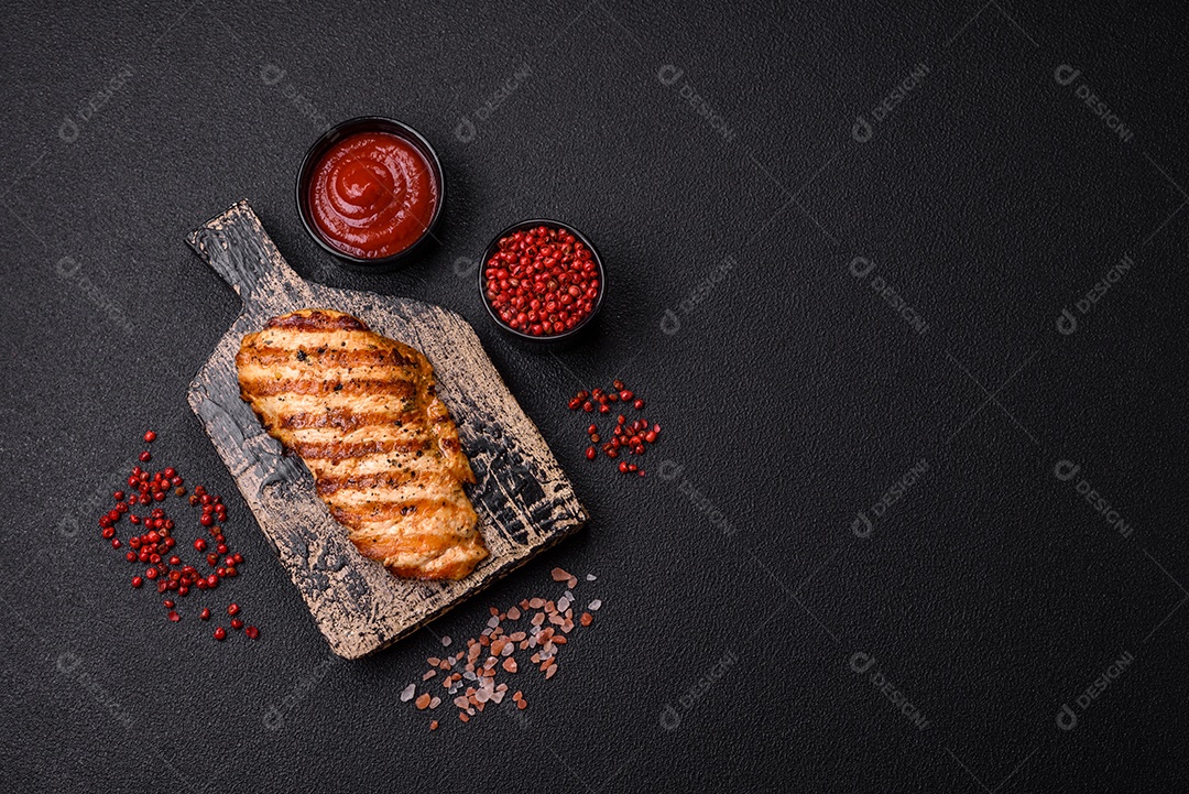 Delicioso filé de frango grelhado fresco com especiarias e ervas em um fundo escuro de concreto. Um prato cozido no fogo