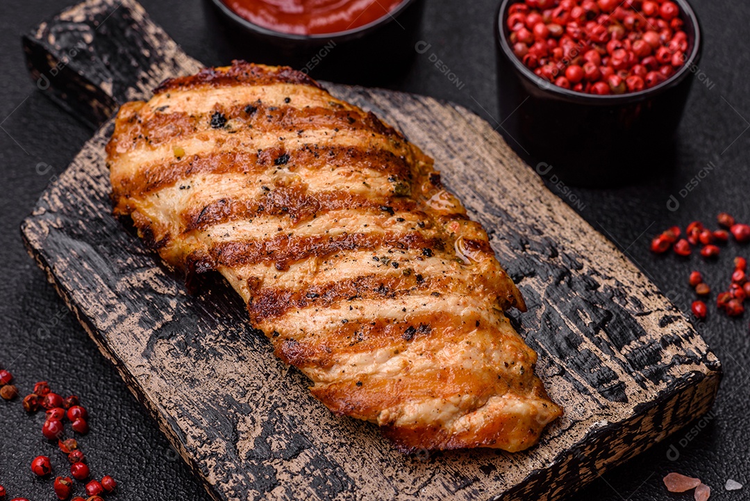 Delicioso filé de frango grelhado fresco com especiarias e ervas em um fundo escuro de concreto. Um prato cozido no fogo