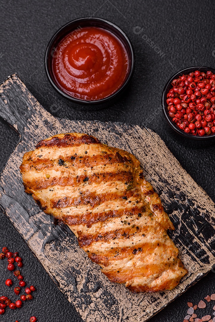 Delicioso filé de frango grelhado fresco com especiarias e ervas em um fundo escuro de concreto. Um prato cozido no fogo