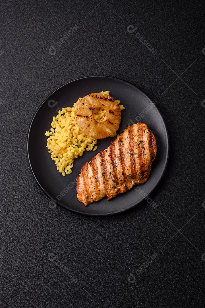 Delicioso filé de frango grelhado fresco com especiarias e ervas em um fundo escuro de concreto. Um prato cozido no fogo