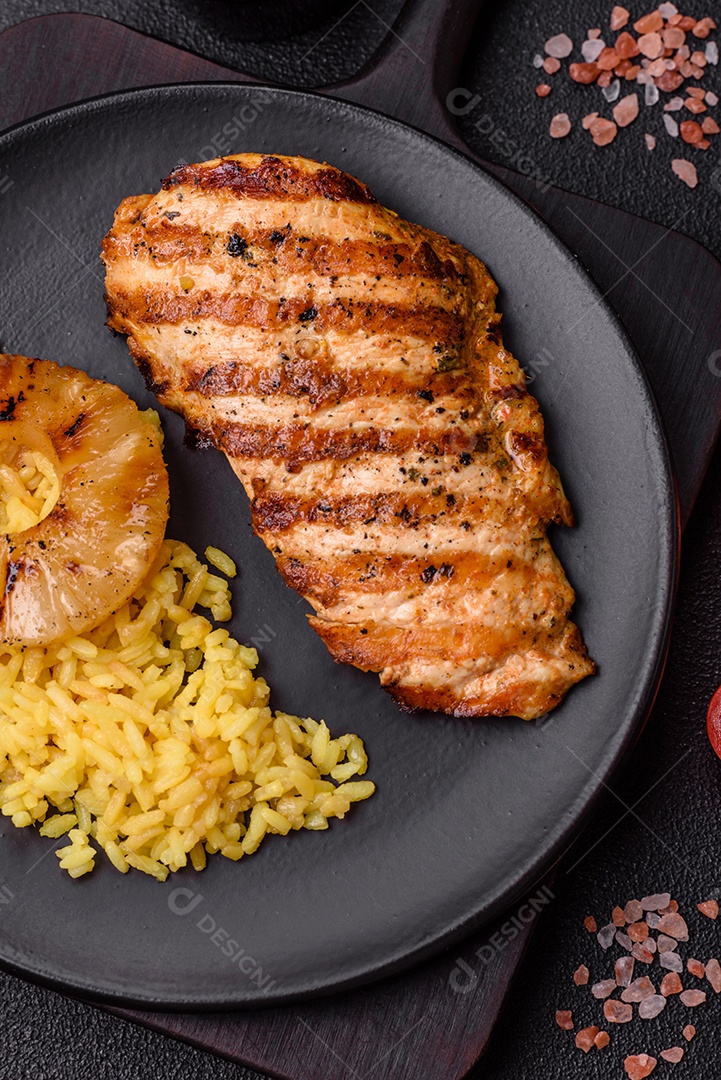 Delicioso filé de frango grelhado fresco com especiarias e ervas em um fundo escuro de concreto. Um prato cozido no fogo