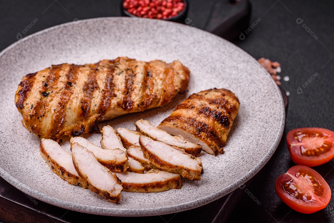 Delicioso filé de frango grelhado fresco com especiarias e ervas em um fundo escuro de concreto. Um prato cozido no fogo