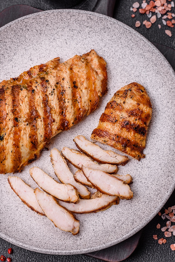 Delicioso filé de frango grelhado fresco com especiarias e ervas em um fundo escuro de concreto. Um prato cozido no fogo