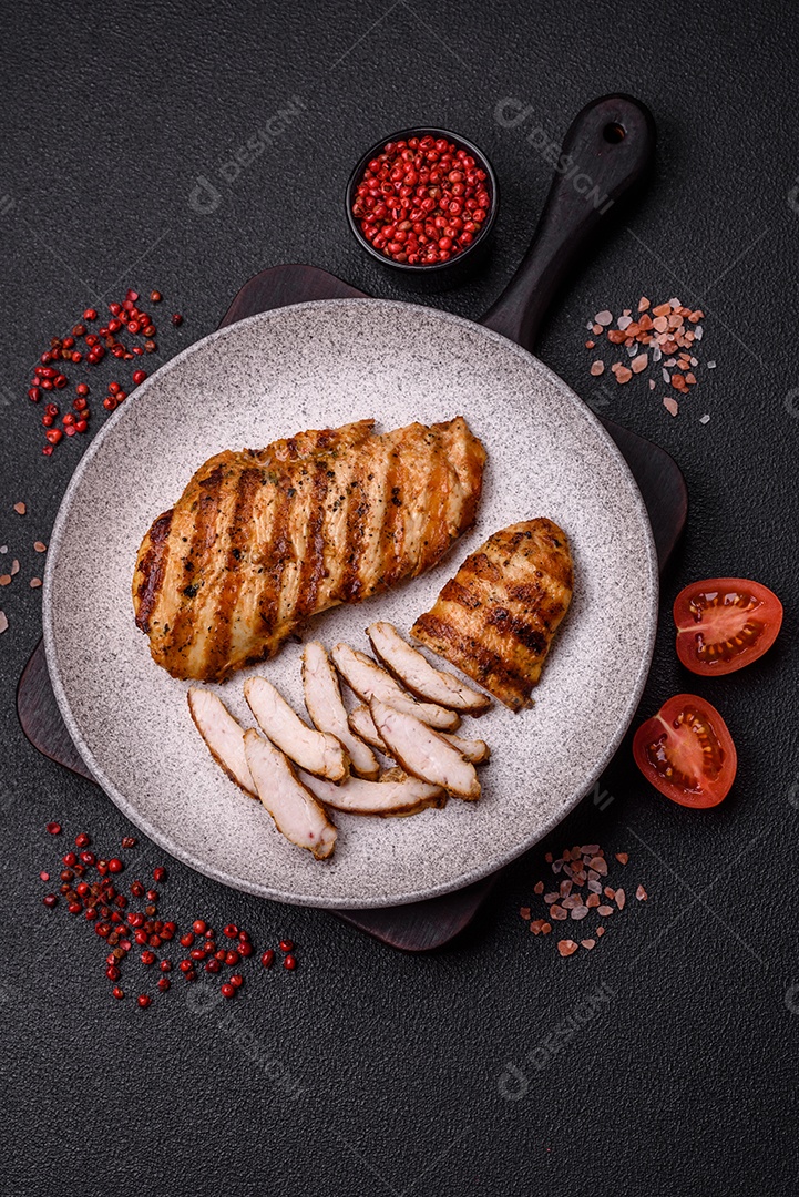 Delicioso filé de frango grelhado fresco com especiarias e ervas em um fundo escuro de concreto. Um prato cozido no fogo