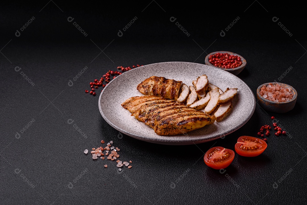 Delicioso filé de frango grelhado fresco com especiarias e ervas em um fundo escuro de concreto. Um prato cozido no fogo