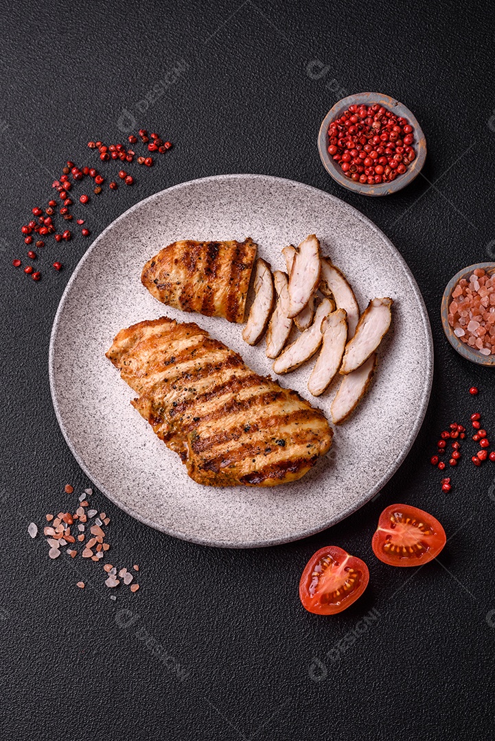 Delicioso filé de frango grelhado fresco com especiarias e ervas em um fundo escuro de concreto. Um prato cozido no fogo