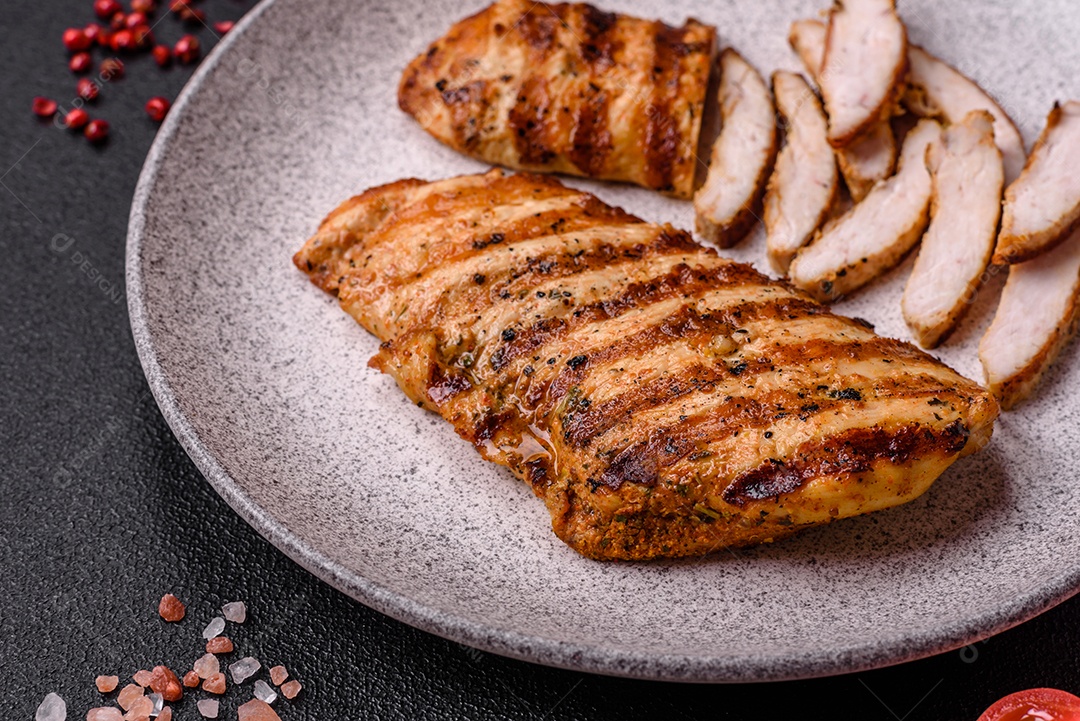 Delicioso filé de frango grelhado fresco com especiarias e ervas em um fundo escuro de concreto. Um prato cozido no fogo