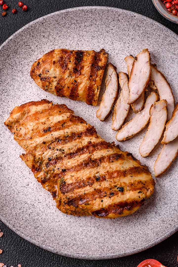 Delicioso filé de frango grelhado fresco com especiarias e ervas em um fundo escuro de concreto. Um prato cozido no fogo