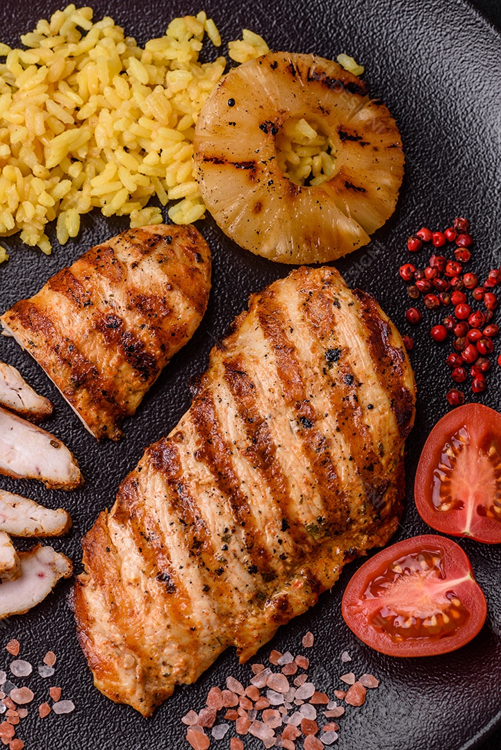 Delicioso filé de frango grelhado fresco com especiarias e ervas em um fundo escuro de concreto. Um prato cozido no fogo
