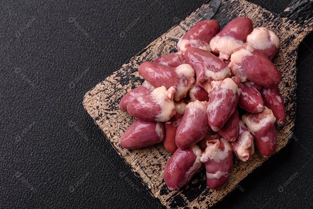 Corações de frango cru com sal, especiarias e ervas sobre um fundo escuro de concreto