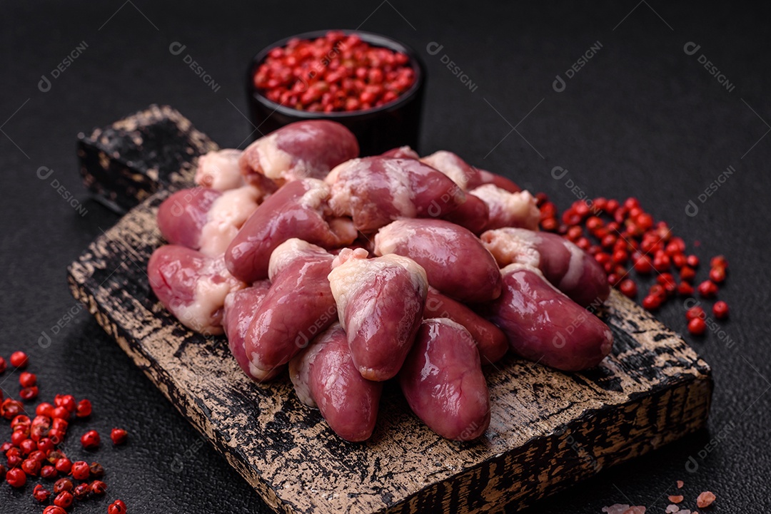 Corações de frango cru com sal, especiarias e ervas sobre um fundo escuro de concreto