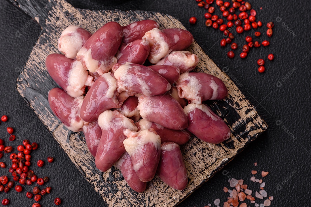 Corações de frango cru com sal, especiarias e ervas sobre um fundo escuro de concreto
