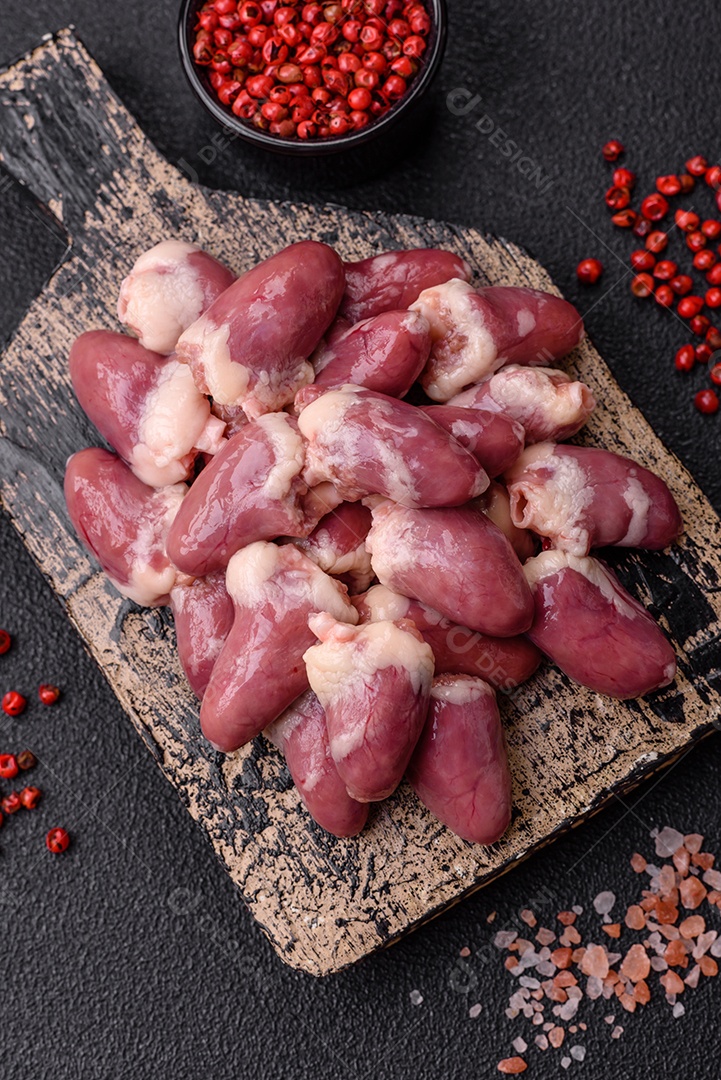 Corações de frango cru com sal, especiarias e ervas sobre um fundo escuro de concreto