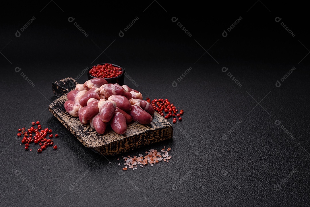 Corações de frango cru com sal, especiarias e ervas sobre um fundo escuro de concreto