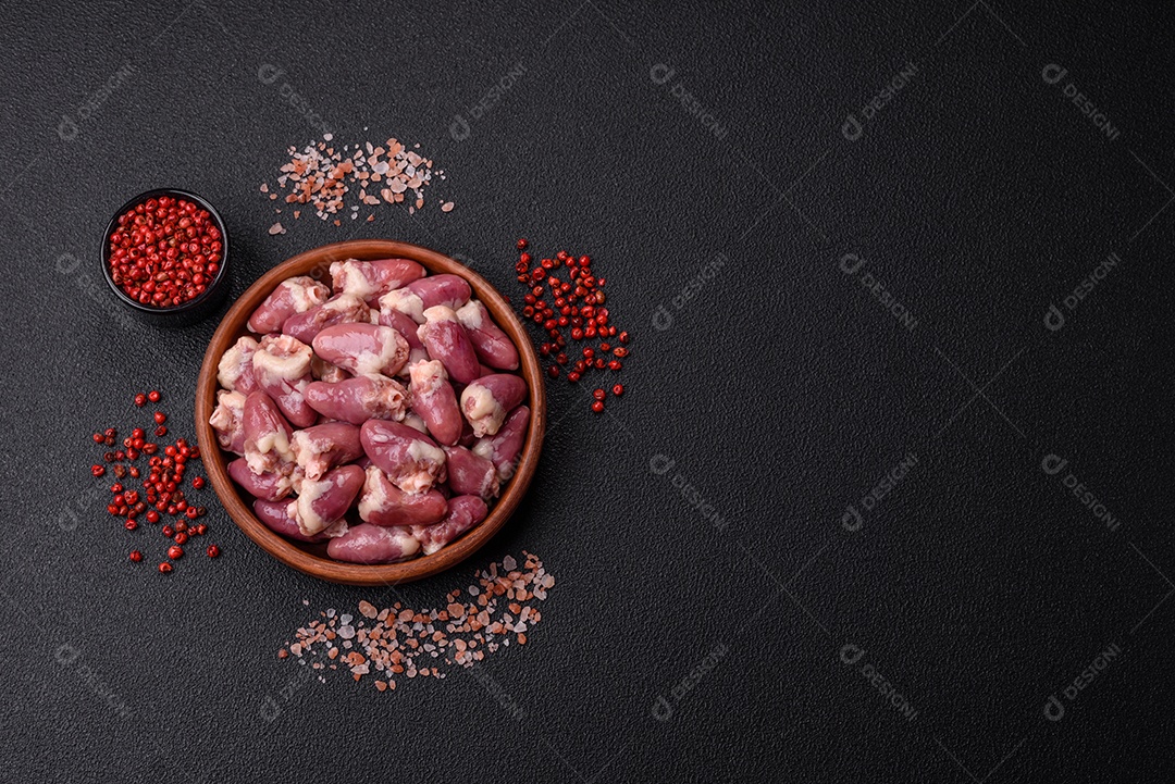 Corações de frango cru com sal, especiarias e ervas sobre um fundo escuro de concreto