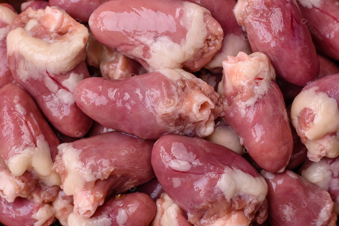 Corações de frango cru com sal, especiarias e ervas sobre um fundo escuro de concreto