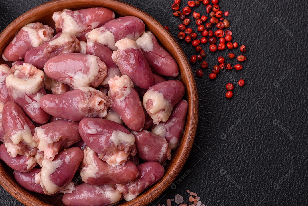 Corações de frango cru com sal, especiarias e ervas sobre um fundo escuro de concreto