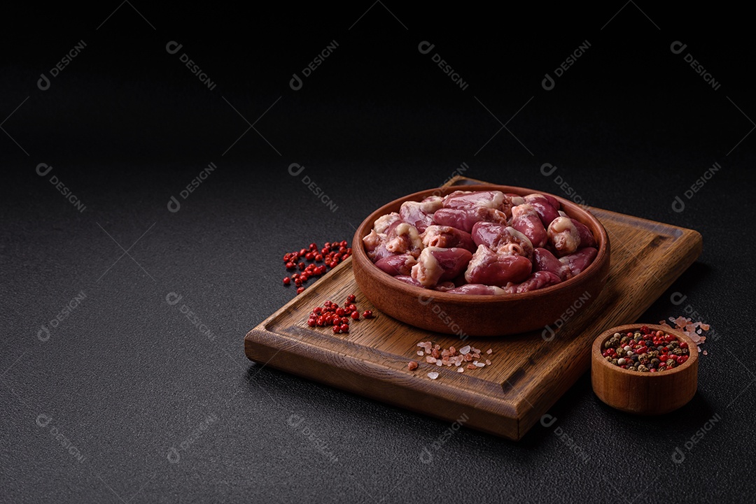 Corações de frango cru com sal, especiarias e ervas sobre um fundo escuro de concreto