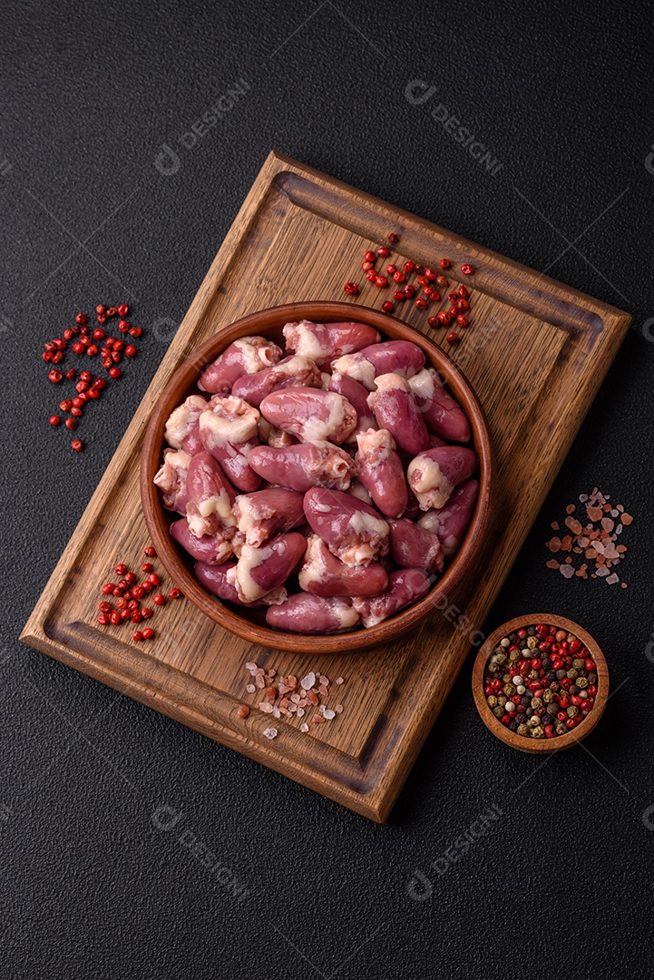 Corações de frango cru com sal, especiarias e ervas sobre um fundo escuro de concreto