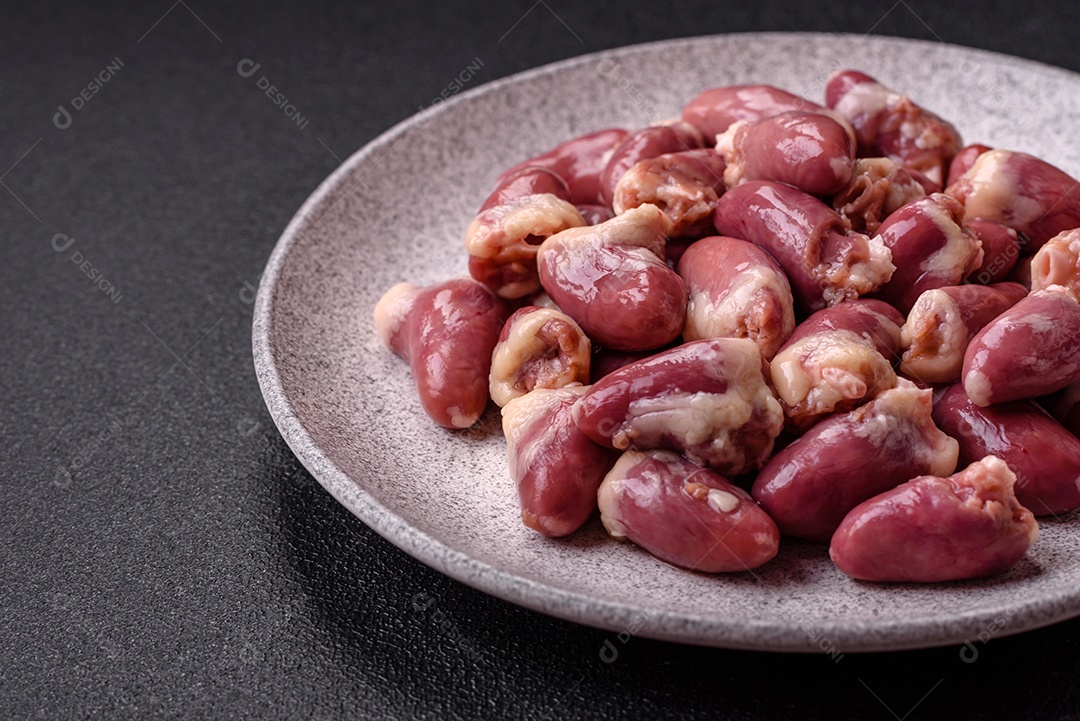 Corações de frango cru com sal, especiarias e ervas sobre um fundo escuro de concreto