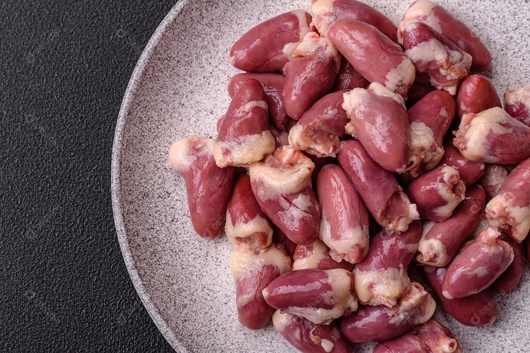 Corações de frango cru com sal, especiarias e ervas sobre um fundo escuro de concreto