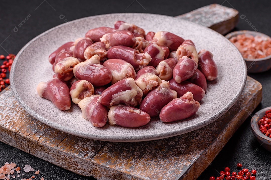 Corações de frango cru com sal, especiarias e ervas sobre um fundo escuro de concreto