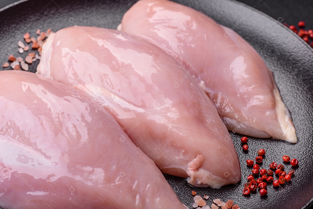 Fatias de frango cru ou filé de peru com sal, especiarias e ervas sobre um fundo escuro de concreto