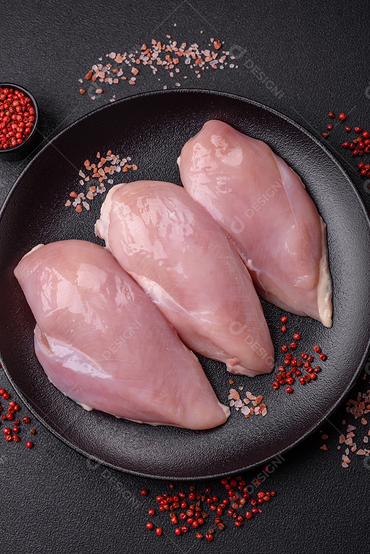 Fatias de frango cru ou filé de peru com sal, especiarias e ervas sobre um fundo escuro de concreto