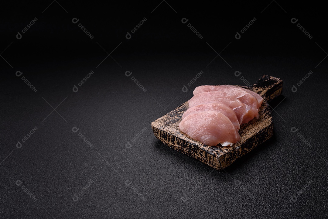 Fatias de frango cru ou filé de peru com sal, especiarias e ervas sobre um fundo escuro de concreto