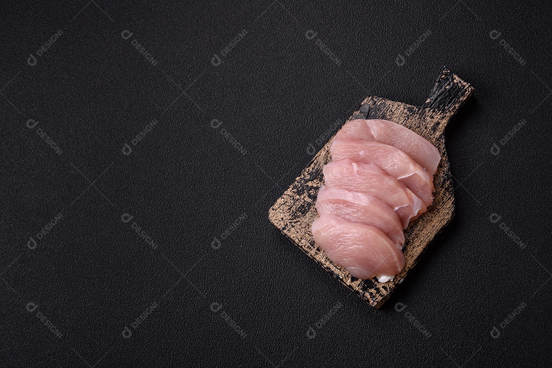 Fatias de frango cru ou filé de peru com sal, especiarias e ervas sobre um fundo escuro de concreto