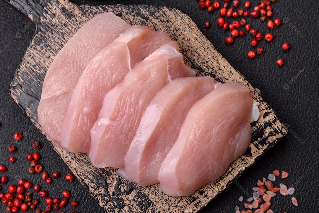 Fatias de frango cru ou filé de peru com sal, especiarias e ervas sobre um fundo escuro de concreto