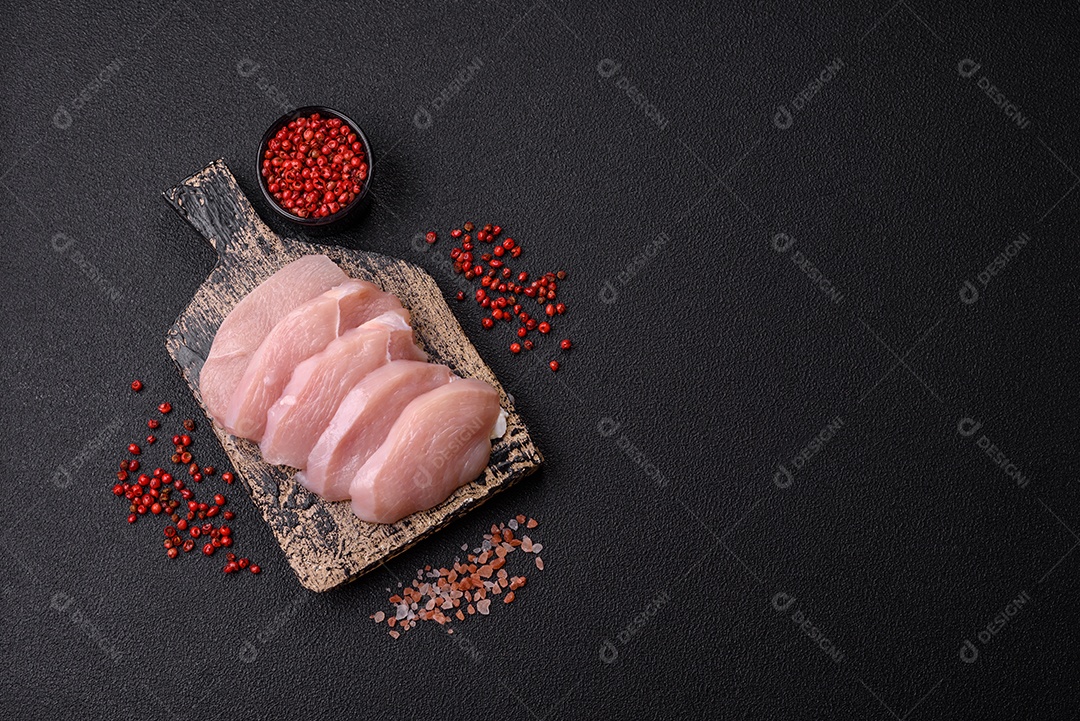 Fatias de frango cru ou filé de peru com sal, especiarias e ervas sobre um fundo escuro de concreto