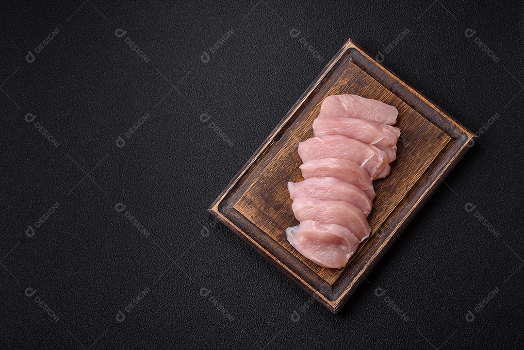 Fatias de frango cru ou filé de peru com sal, especiarias e ervas sobre um fundo escuro de concreto