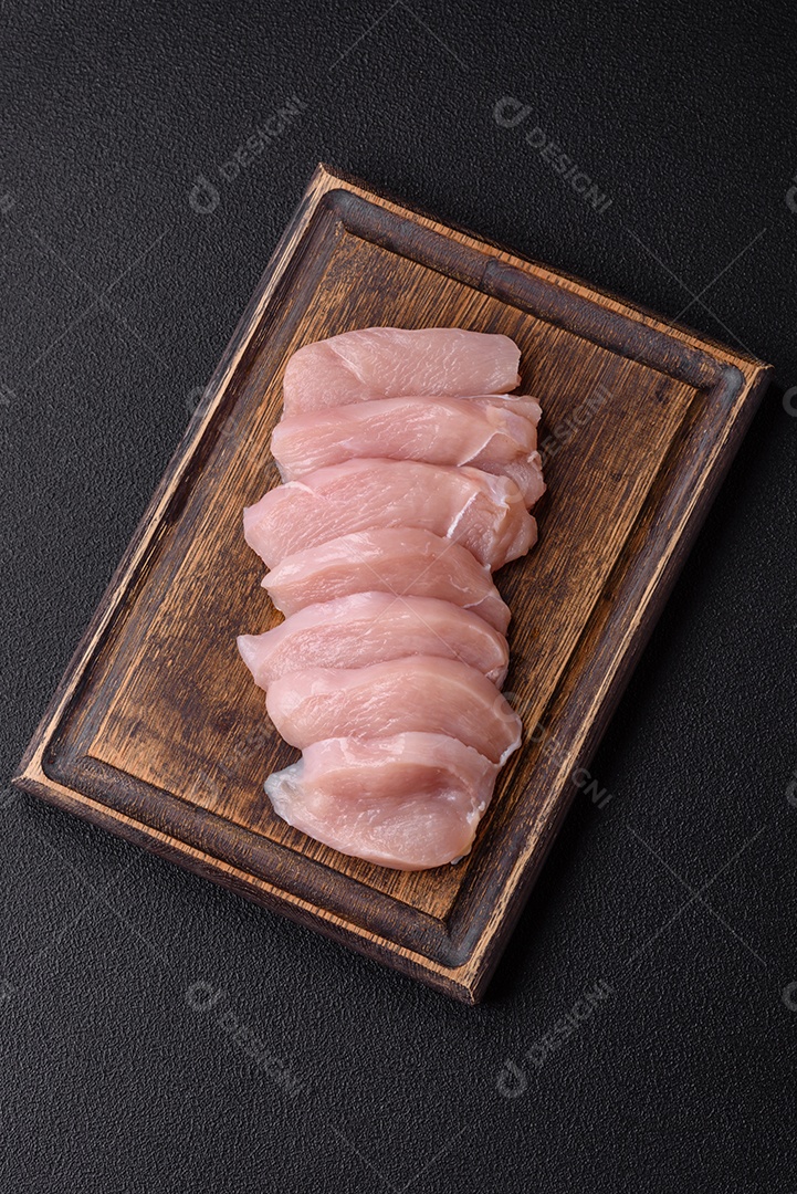 Fatias de frango cru ou filé de peru com sal, especiarias e ervas sobre um fundo escuro de concreto