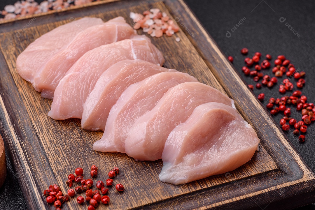 Fatias de frango cru ou filé de peru com sal, especiarias e ervas sobre um fundo escuro de concreto