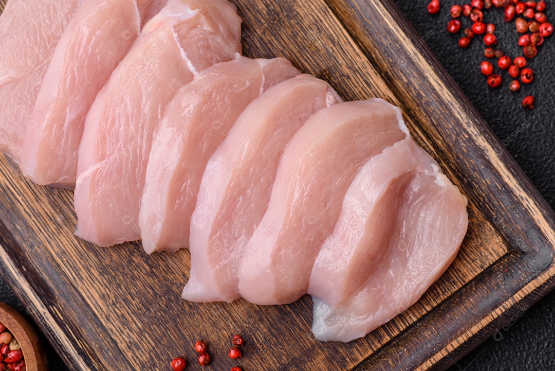 Fatias de frango cru ou filé de peru com sal, especiarias e ervas sobre um fundo escuro de concreto