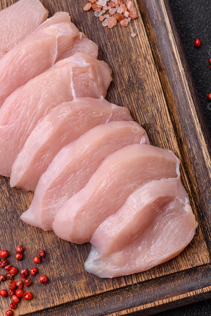 Fatias de frango cru ou filé de peru com sal, especiarias e ervas sobre um fundo escuro de concreto