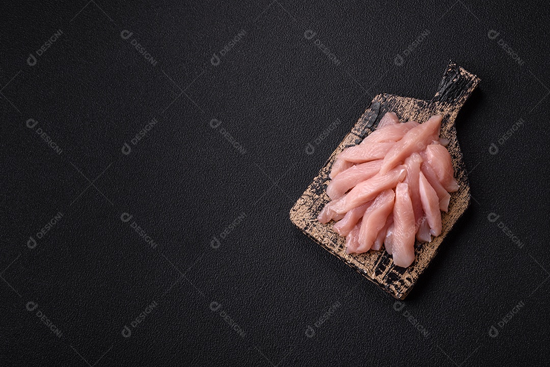 Fatias de frango cru ou filé de peru com sal, especiarias e ervas sobre um fundo escuro de concreto