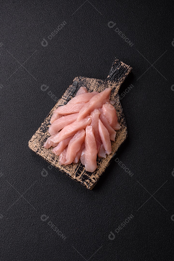 Fatias de frango cru ou filé de peru com sal, especiarias e ervas sobre um fundo escuro de concreto