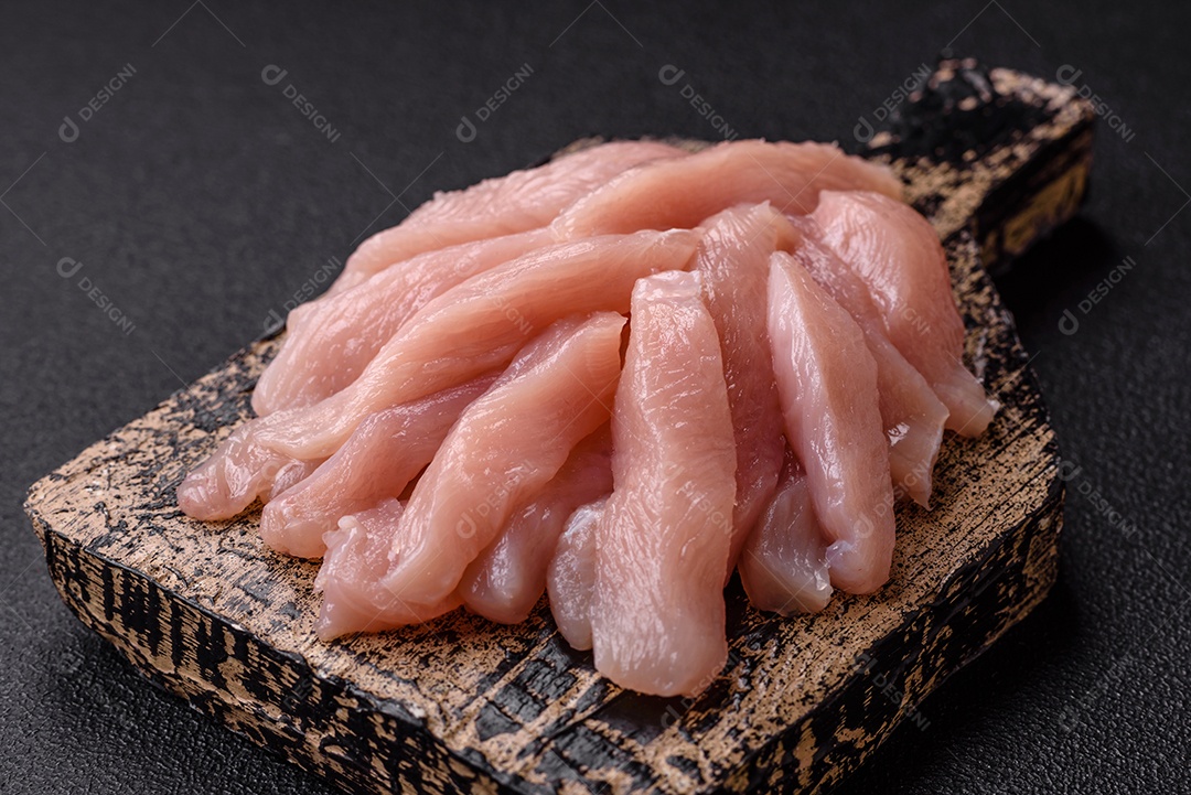 Fatias de frango cru ou filé de peru com sal, especiarias e ervas sobre um fundo escuro de concreto