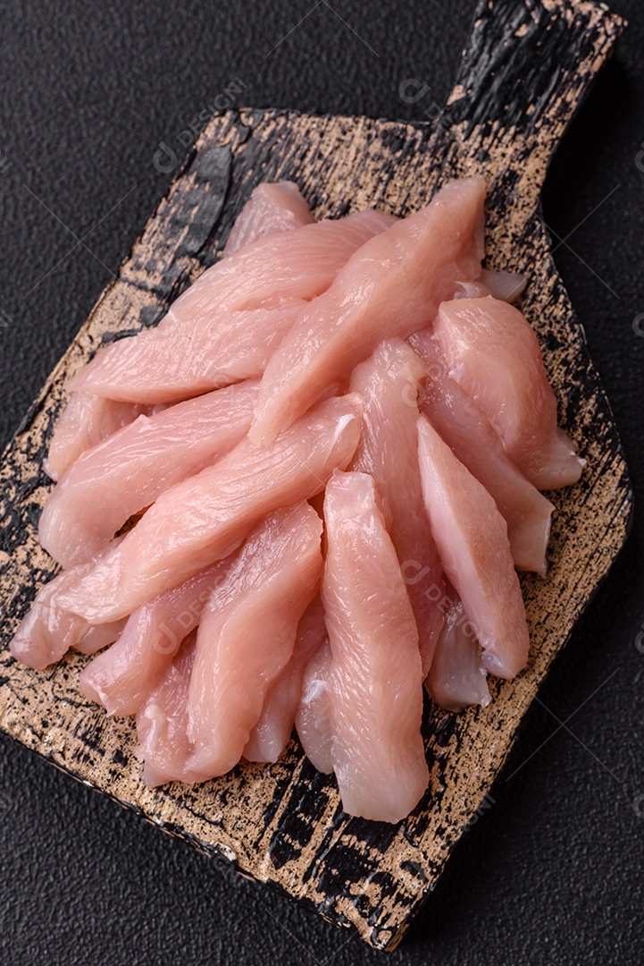 Fatias de frango cru ou filé de peru com sal, especiarias e ervas sobre um fundo escuro de concreto