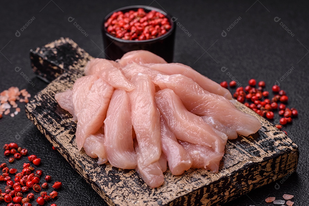 Fatias de frango cru ou filé de peru com sal, especiarias e ervas sobre um fundo escuro de concreto