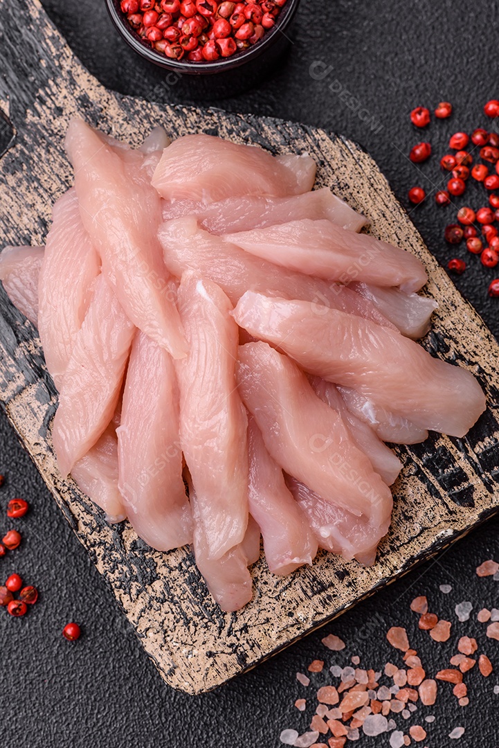 Fatias de frango cru ou filé de peru com sal, especiarias e ervas sobre um fundo escuro de concreto