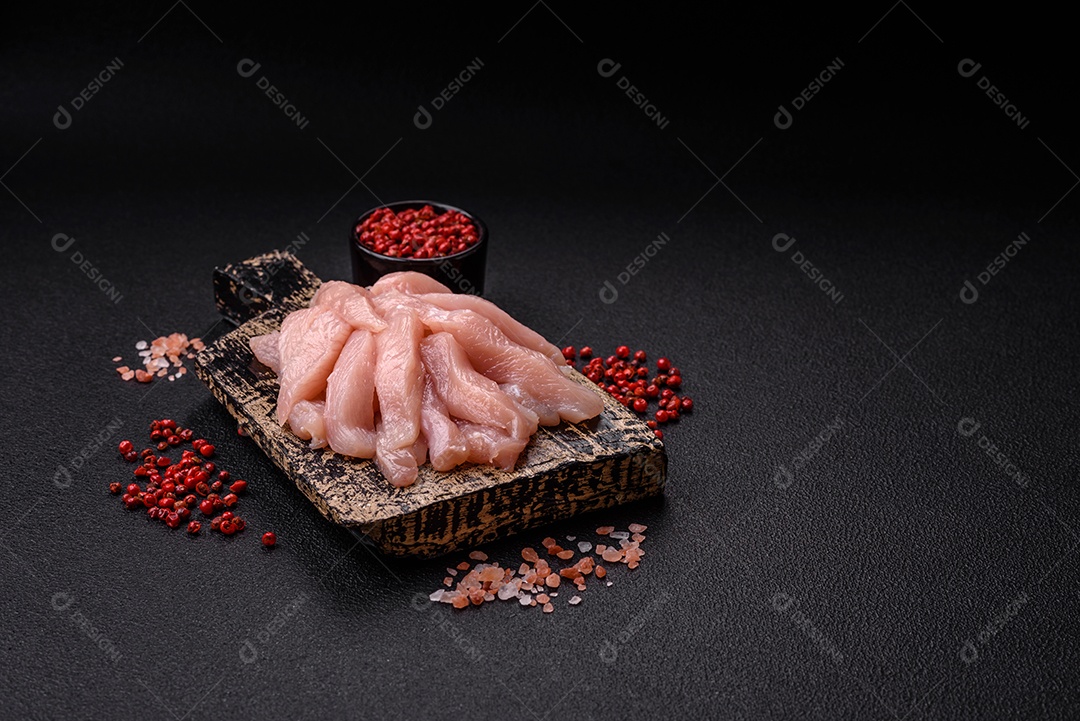 Fatias de frango cru ou filé de peru com sal, especiarias e ervas sobre um fundo escuro de concreto