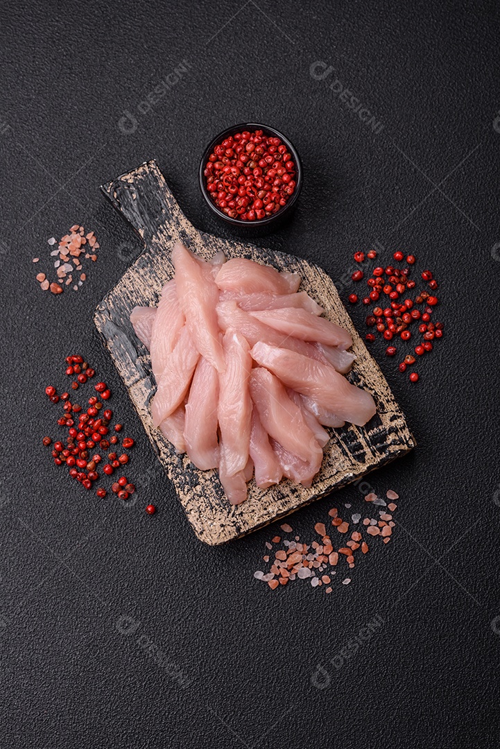 Fatias de frango cru ou filé de peru com sal, especiarias e ervas sobre um fundo escuro de concreto